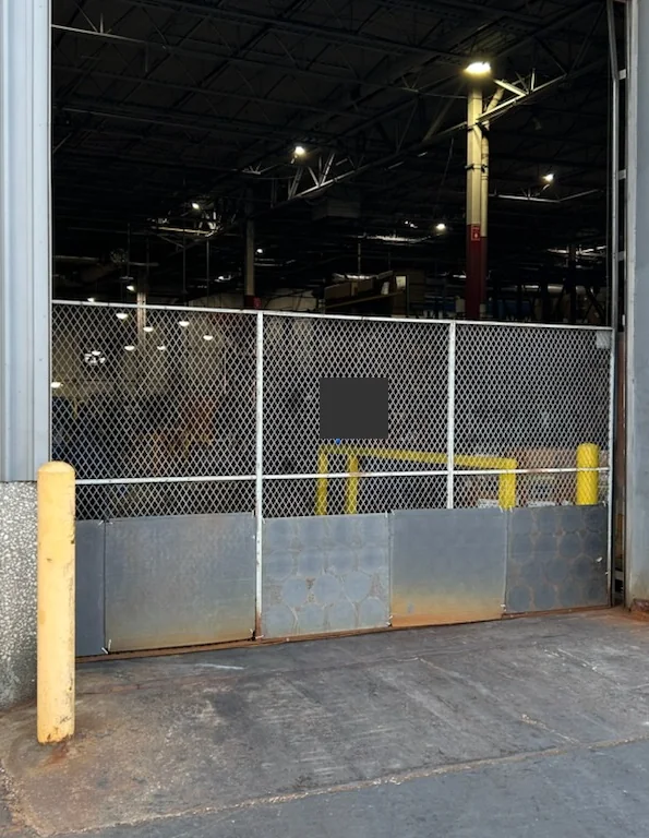 Original warehouse mesh gate with corrosion along its solid lower section.
