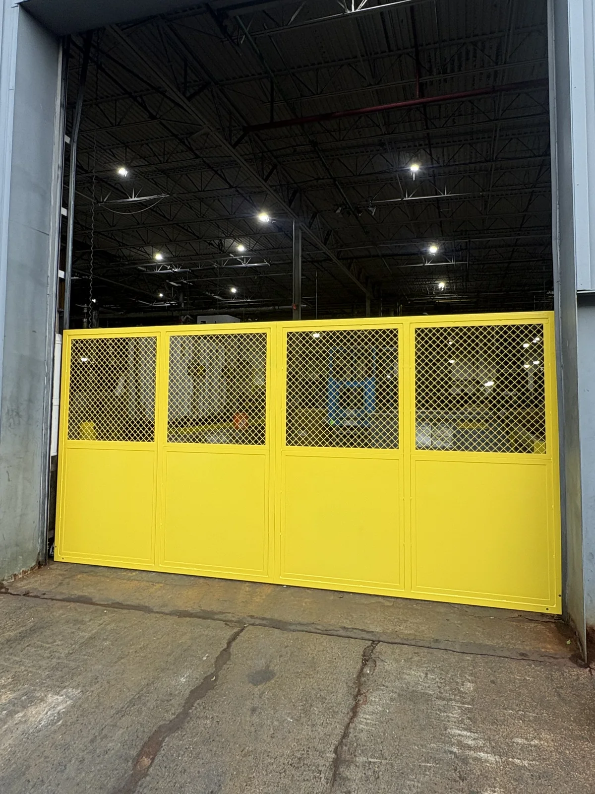 Yellow warehouse gate with mesh upper panels and a solid lower section in Livonia.