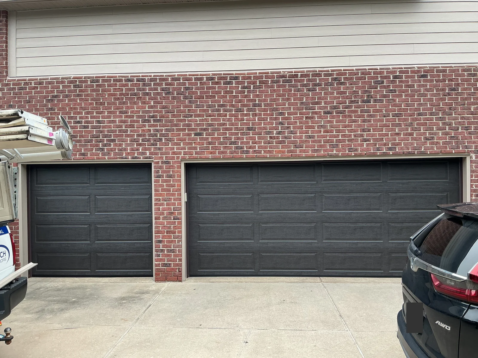 Matching dark single and double garage doors with long raised panels on a brick home in Novi.